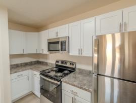 Renovated kitchen featuring white shaker cabinets, stainless steel appliances including refrigerator, oven, and microwave, plus granite-style countertops with ample workspace.
