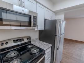 Modern kitchen at Huntley Ridge East featuring stainless steel appliances, including a microwave, refrigerator, and stove with smooth countertops and white cabinetry.