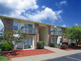 Two-story apartment building with brick and siding exterior, private balconies and patios, and landscaped grounds with trimmed shrubs, trees, and mulch beds